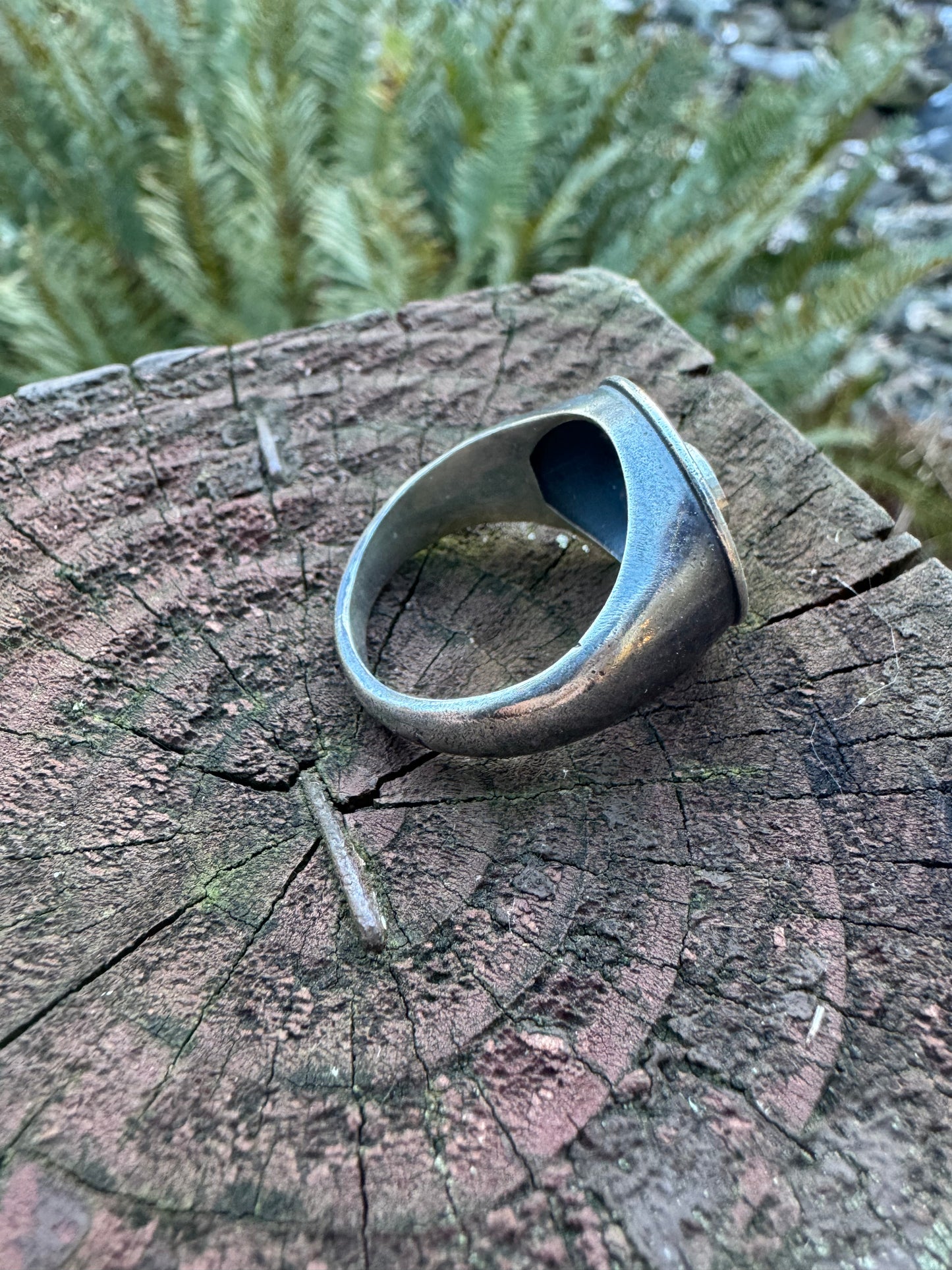 bottom side of a silver ring with a floral design displayed on a wood surface, set against a outdoor scene