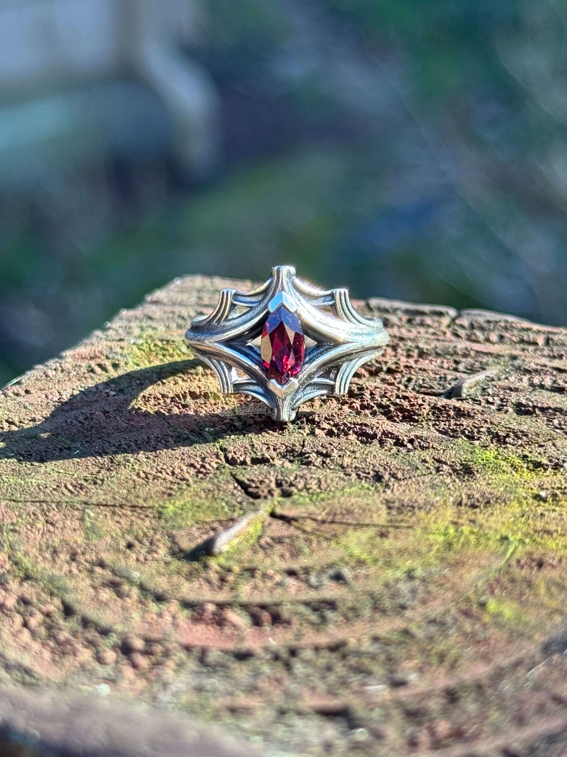 Silver ring with an ornate design featuring a large marquise-cut red gemstone, displayed on a textured wooden surface