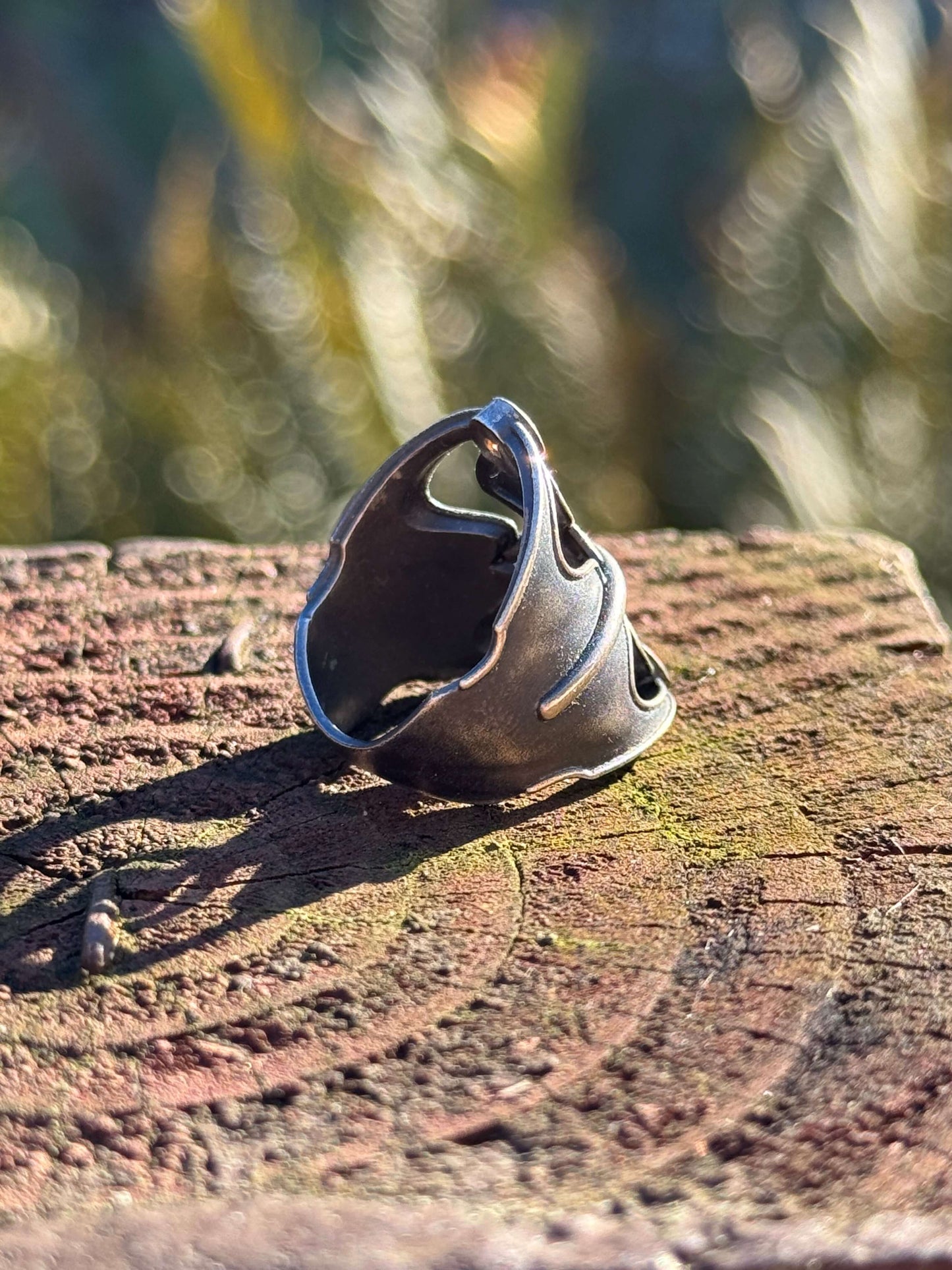 Silver ring with an abstract design featuring two orange gemstones, displayed on a textured wooden surface outdoors.