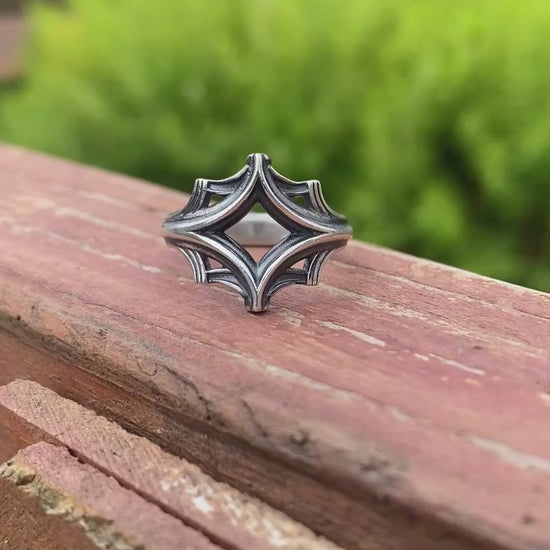 Silver ring with an intricate geometric design, displayed on a wooden surface with a blurred green background