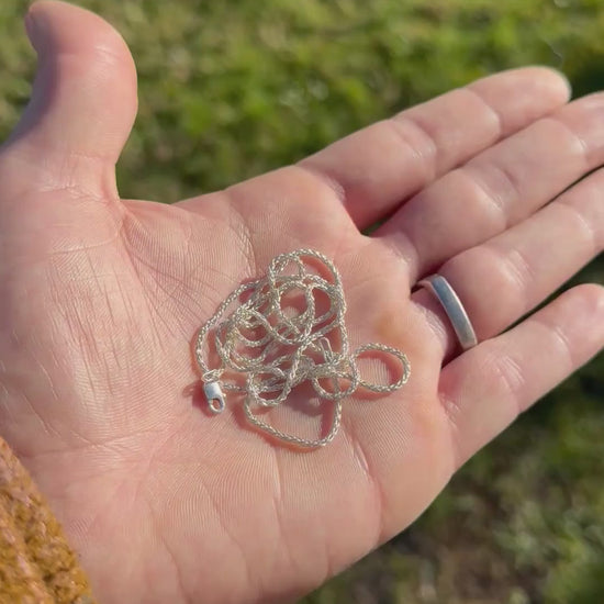 Hand holding a polished coiled silver chain against a grassy background