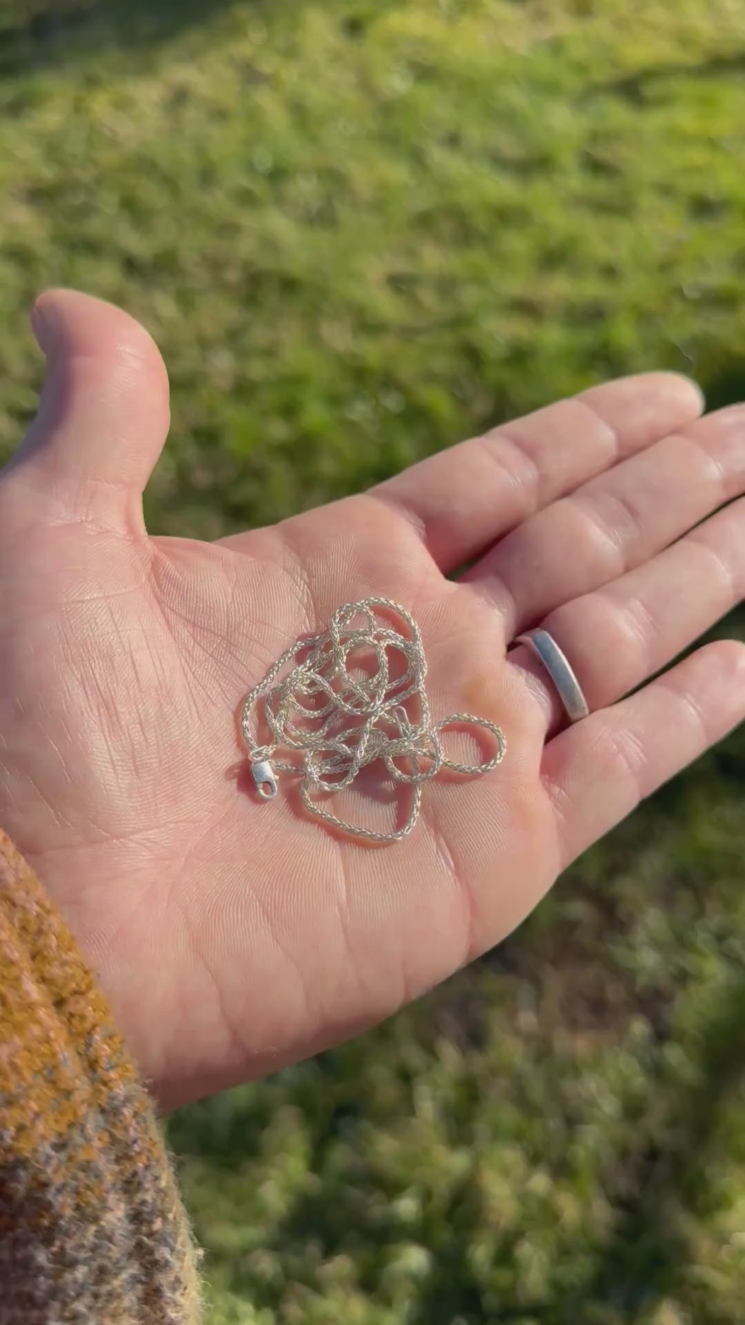 Hand holding a polished coiled silver chain against a grassy background