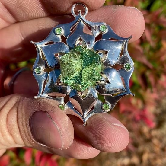 Intricate silver pendant with a floral design, featuring a green central gemstone and smaller green accents