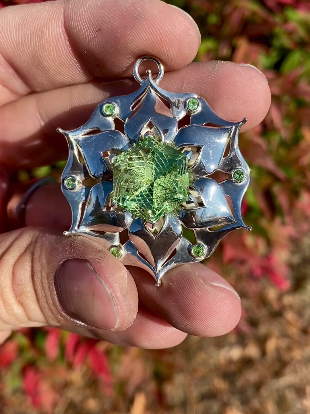 Intricate silver pendant with a floral design, featuring a green central gemstone and smaller green accents