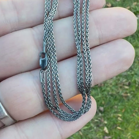 Hand holding a coiled silver chain against a grassy background.